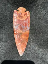 Reverse of the red-orange dovetail flint point showing dark red patches and pale gray veining.